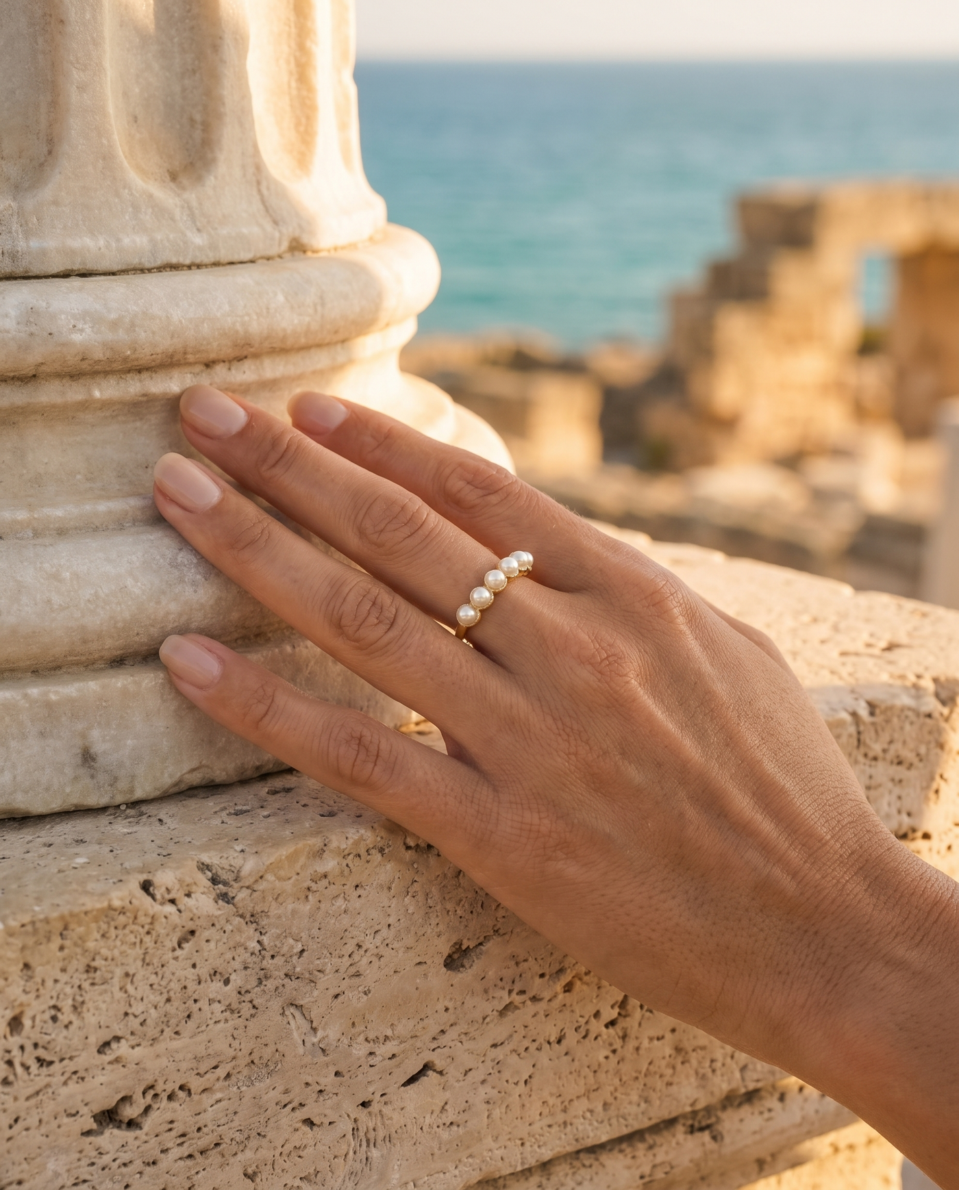 Pearl Cascade Ring worn on a hand by an ancient column overlooking the sea