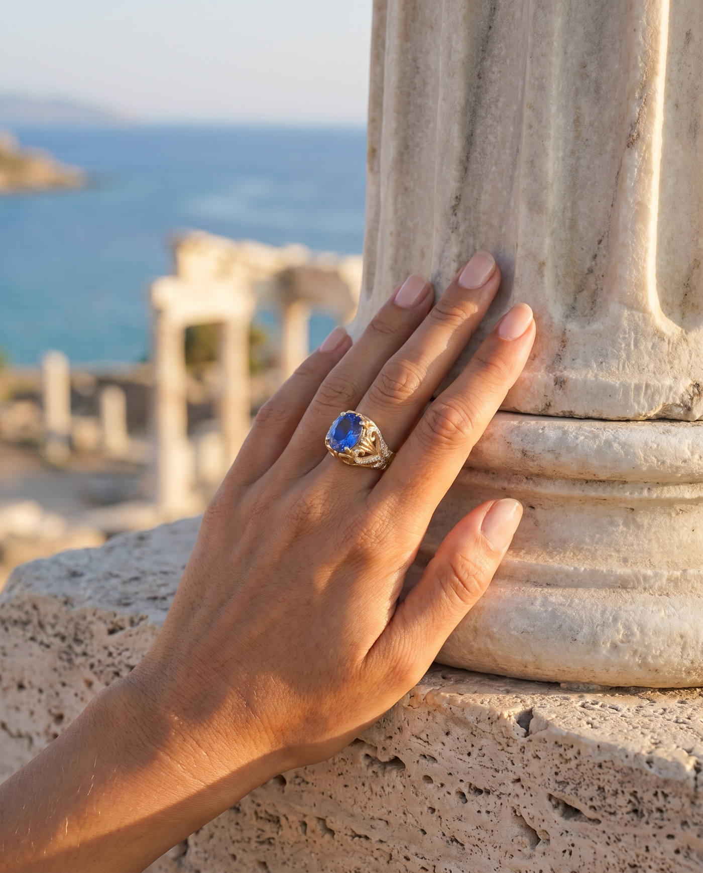 The Aegean Jewel Ring worn on a hand by an ancient column overlooking the sea