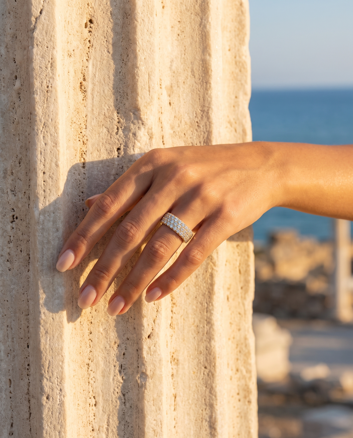 Pave Diamond Infinity Ring worn on a hand by an ancient column overlooking the sea