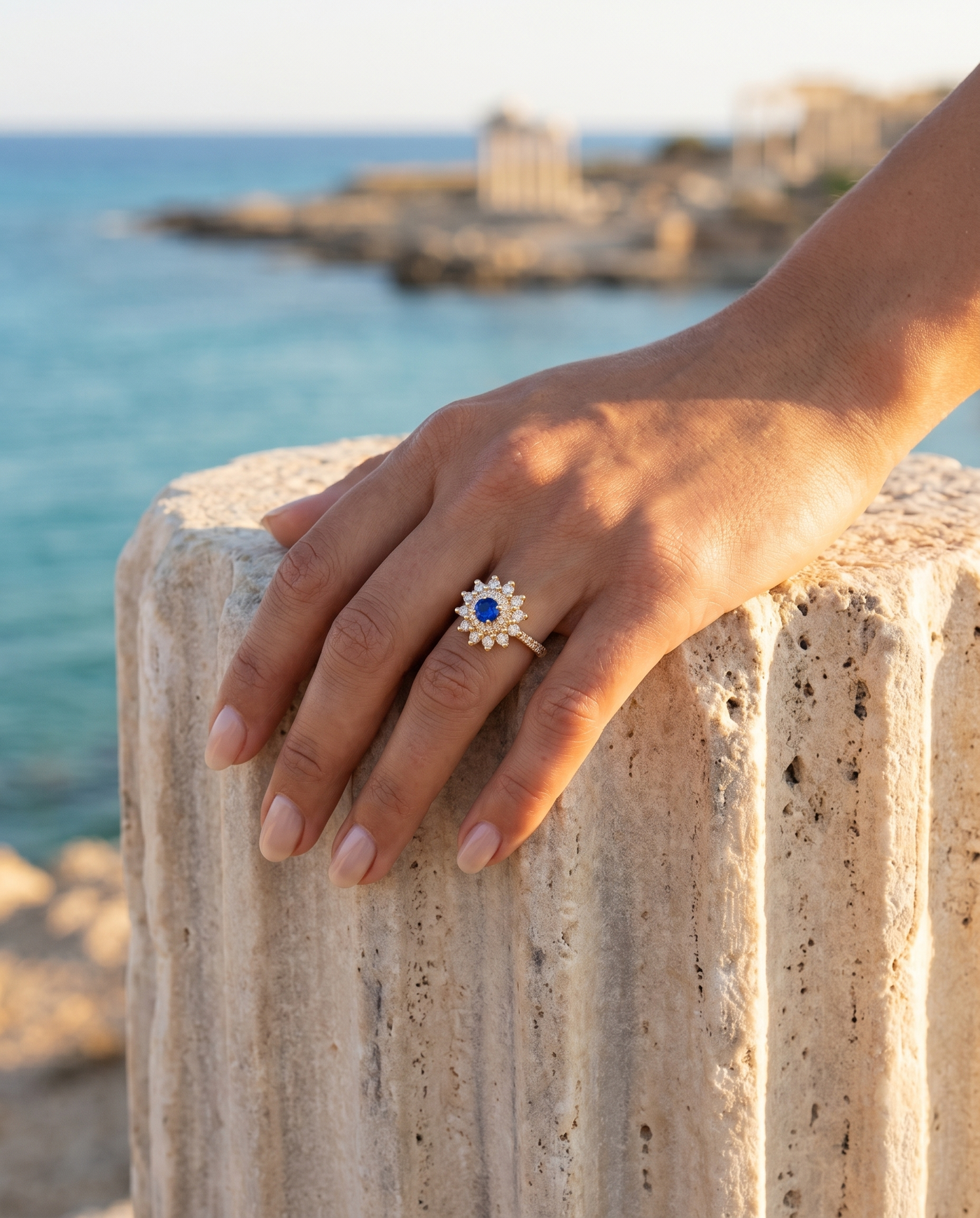 The Fiore Blue Sapphire Ring worn on a hand by an ancient column overlooking the sea