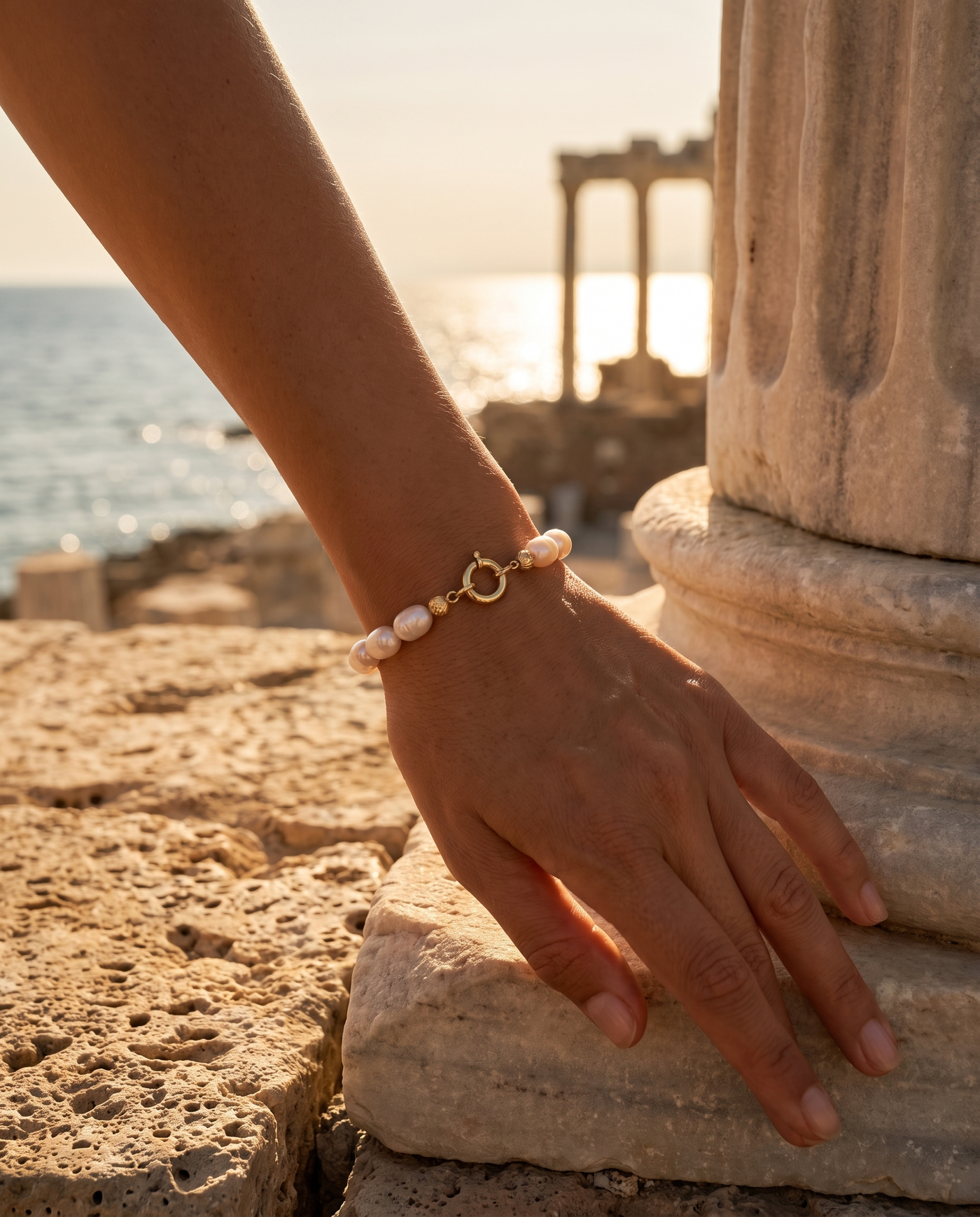 Mediterranean Pearl Bracelet worn on a wrist by an ancient column overlooking the sea