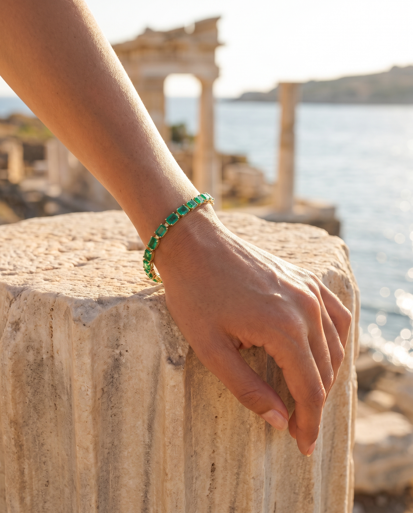 Mykonos Tennis Bracelet Emerald worn on a wrist by an ancient column overlooking the sea