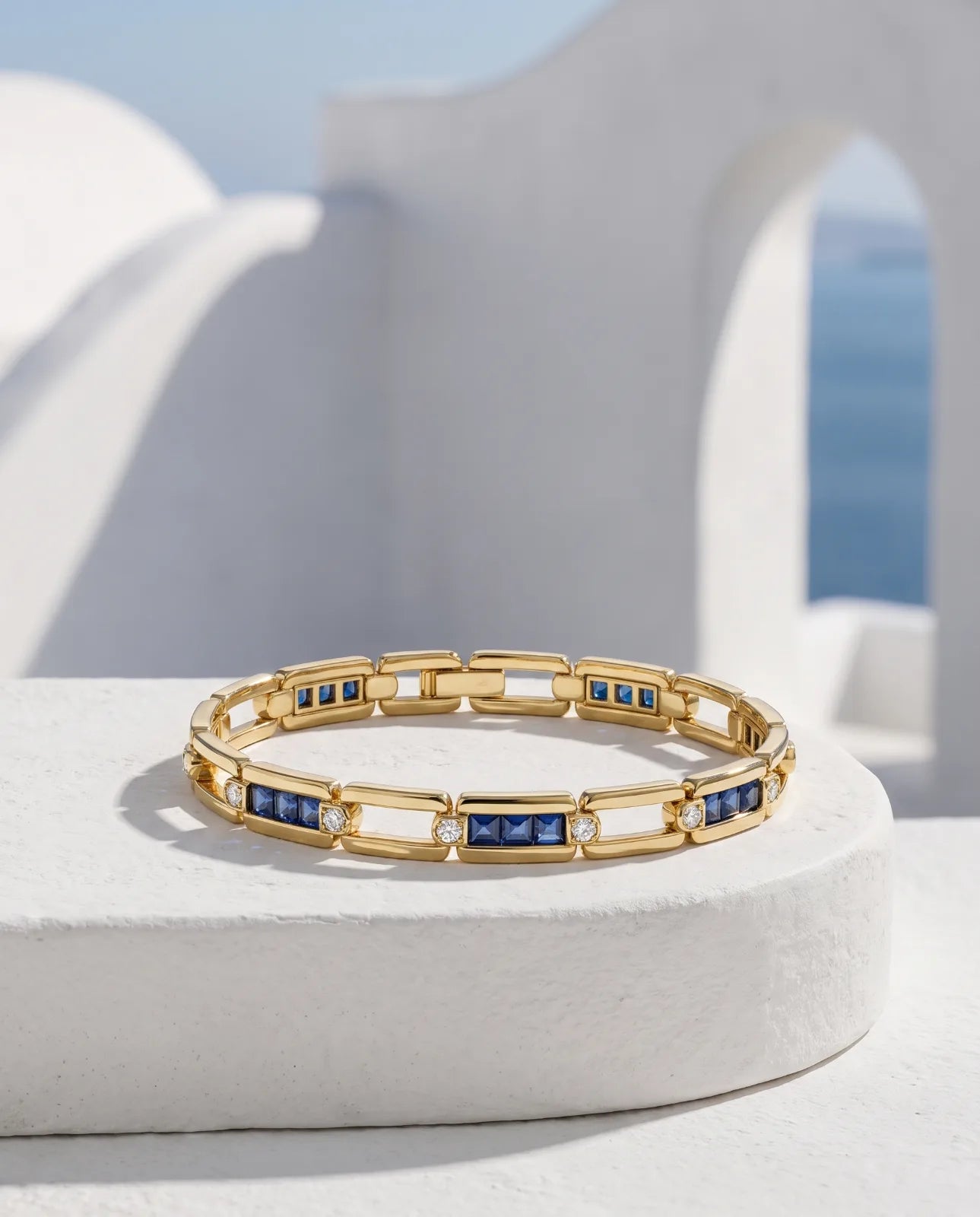 Kastro Bracelet in 14k yellow gold, alternating open rectangular links with channel-set blue sapphire bars capped by bezel diamonds, laid flat in a full loop on a white plinth showing the integrated box clasp
