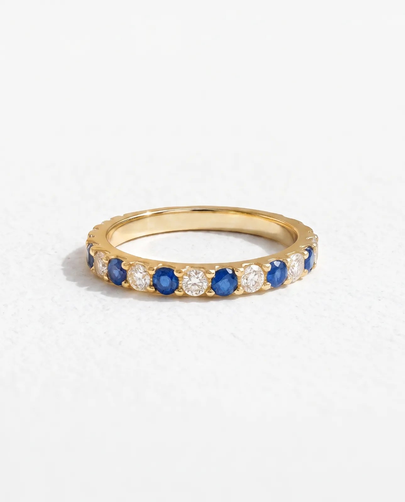 Kyma Band in 14k yellow gold, a half-eternity band alternating round blue sapphires and white diamonds across the crown, shown at a three-quarter angle on a plain white studio background
