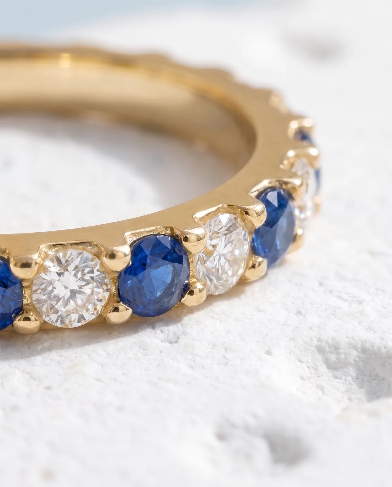 Kyma Band in 14k yellow gold, a half-eternity band alternating round blue sapphires and white diamonds across the crown, in macro detail showing the shared prongs, scalloped edge and smooth unset shank